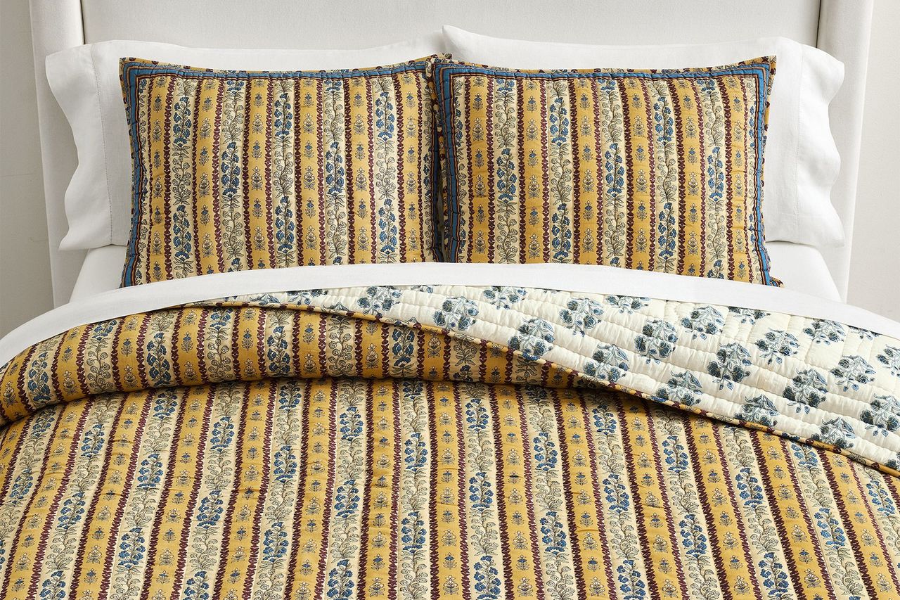 Quilt and matching pillowcases with a striped and floral pattern are displayed on a bed with a white background