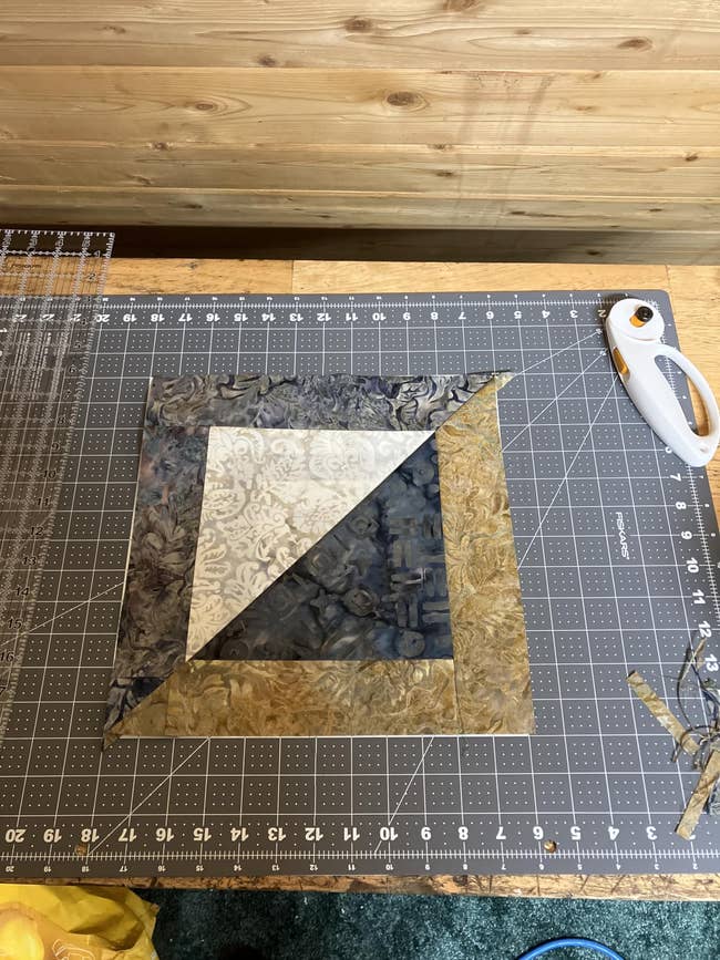 Quilt block with intricate patterns on a cutting mat, surrounded by quilting tools, including a rotary cutter