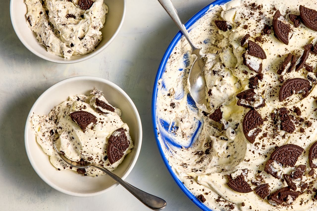 A serving dish and bowls filled with Oreo dessert garnished with cookie pieces and spoons placed beside them