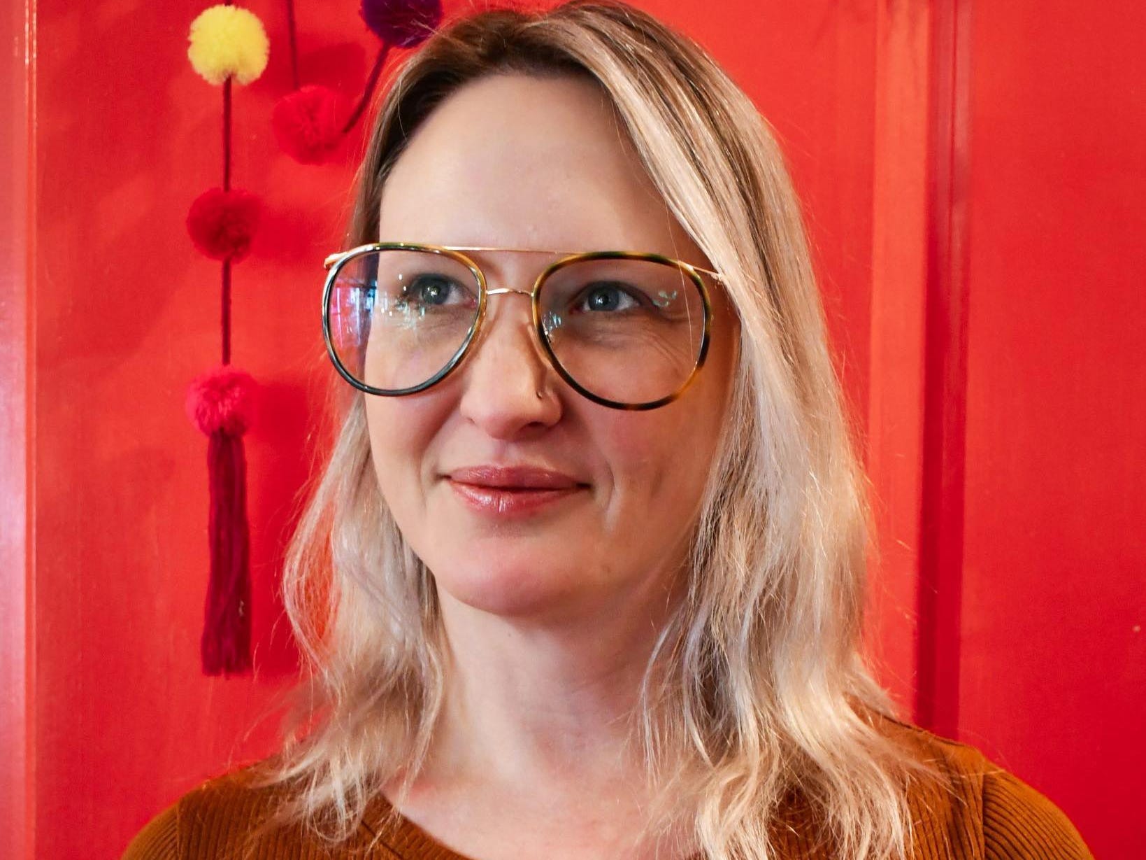 headshot of woman in glasses in front of red background