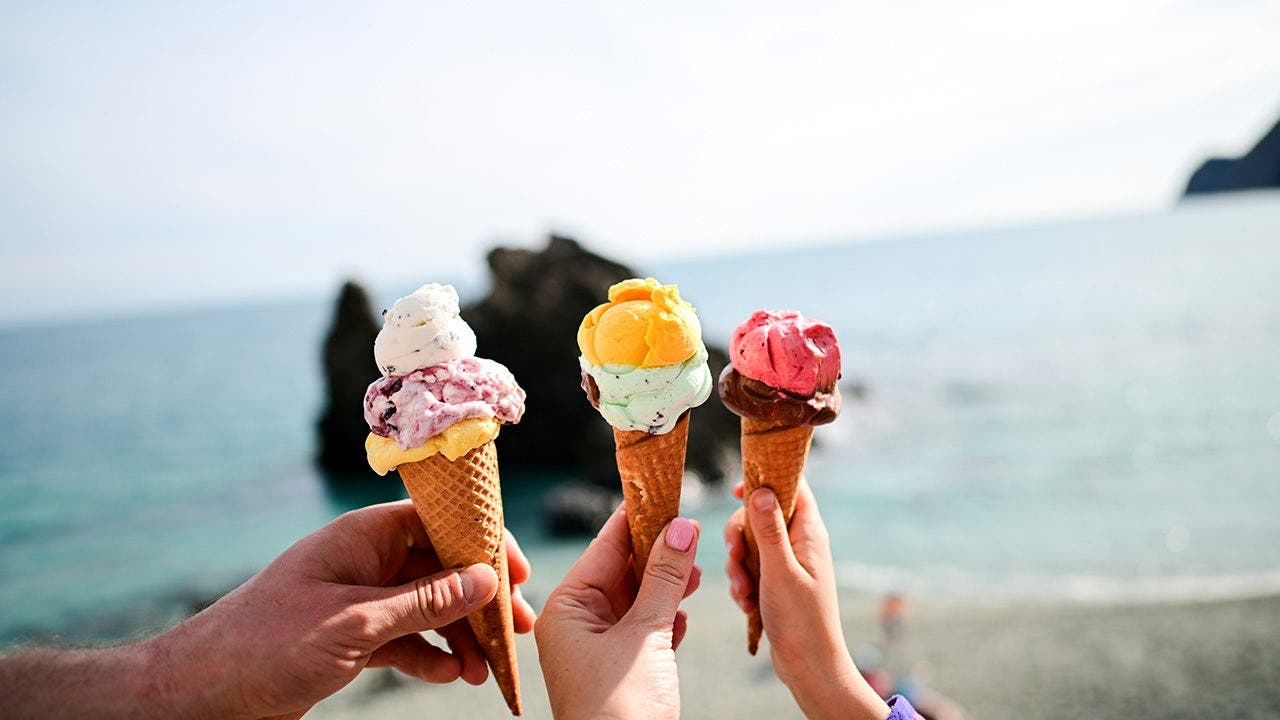 People hold up ice-cream cones beside the ocean.