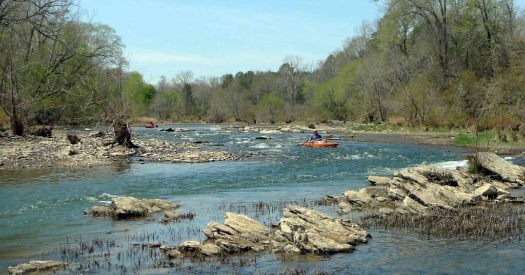A kayaker paddling on the Ouachita River in Arkansas, surrounded by a rocky river bed and woodlands.