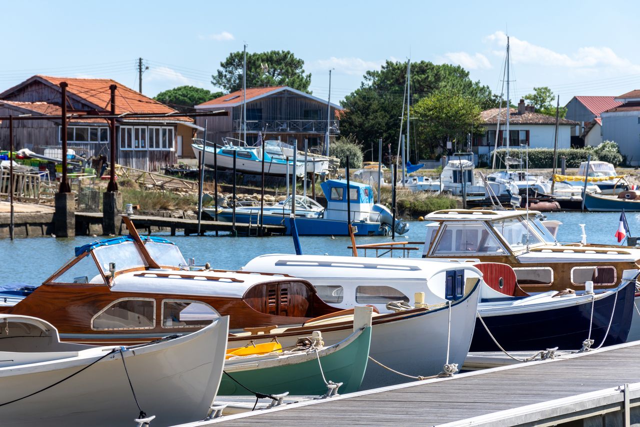 A row of small boats docked in a harbor with houses in the background