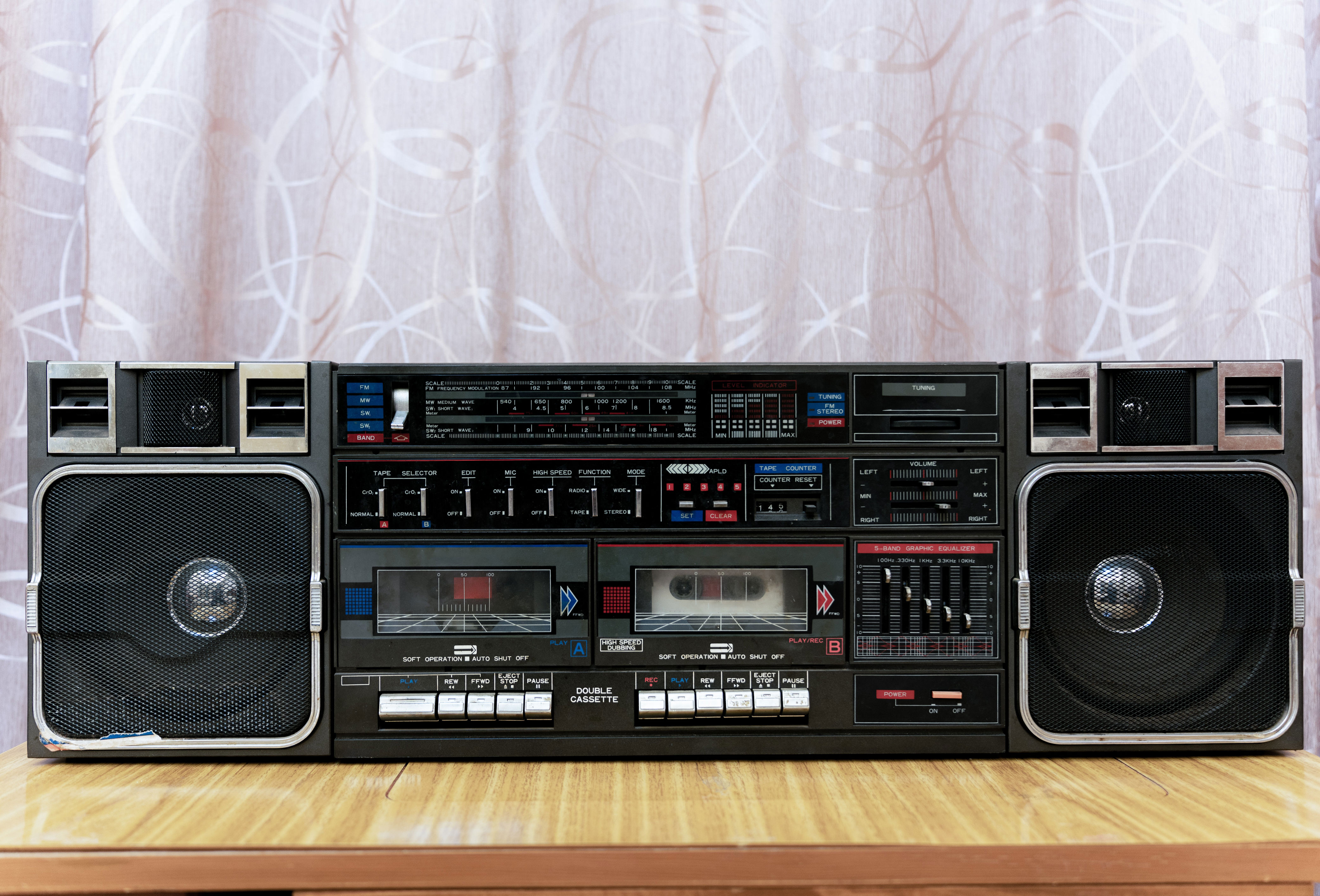 Vintage cassette boombox with two speakers on a wooden surface, set against a patterned curtain backdrop