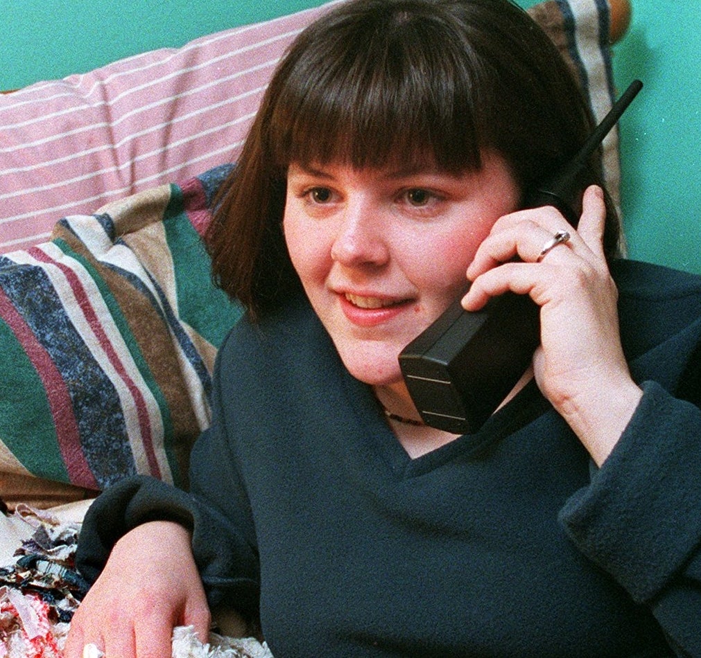 Person on a bed, holding a cordless phone, surrounded by plush toys