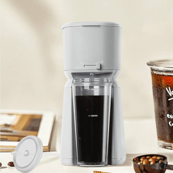 Modern coffee maker with a removable lid, next to a glass of brewed coffee on a table. Ideal for quick home brewing