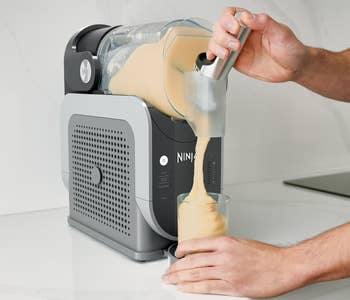 Person pouring a smoothie from a Ninja appliance into a glass in a kitchen setting