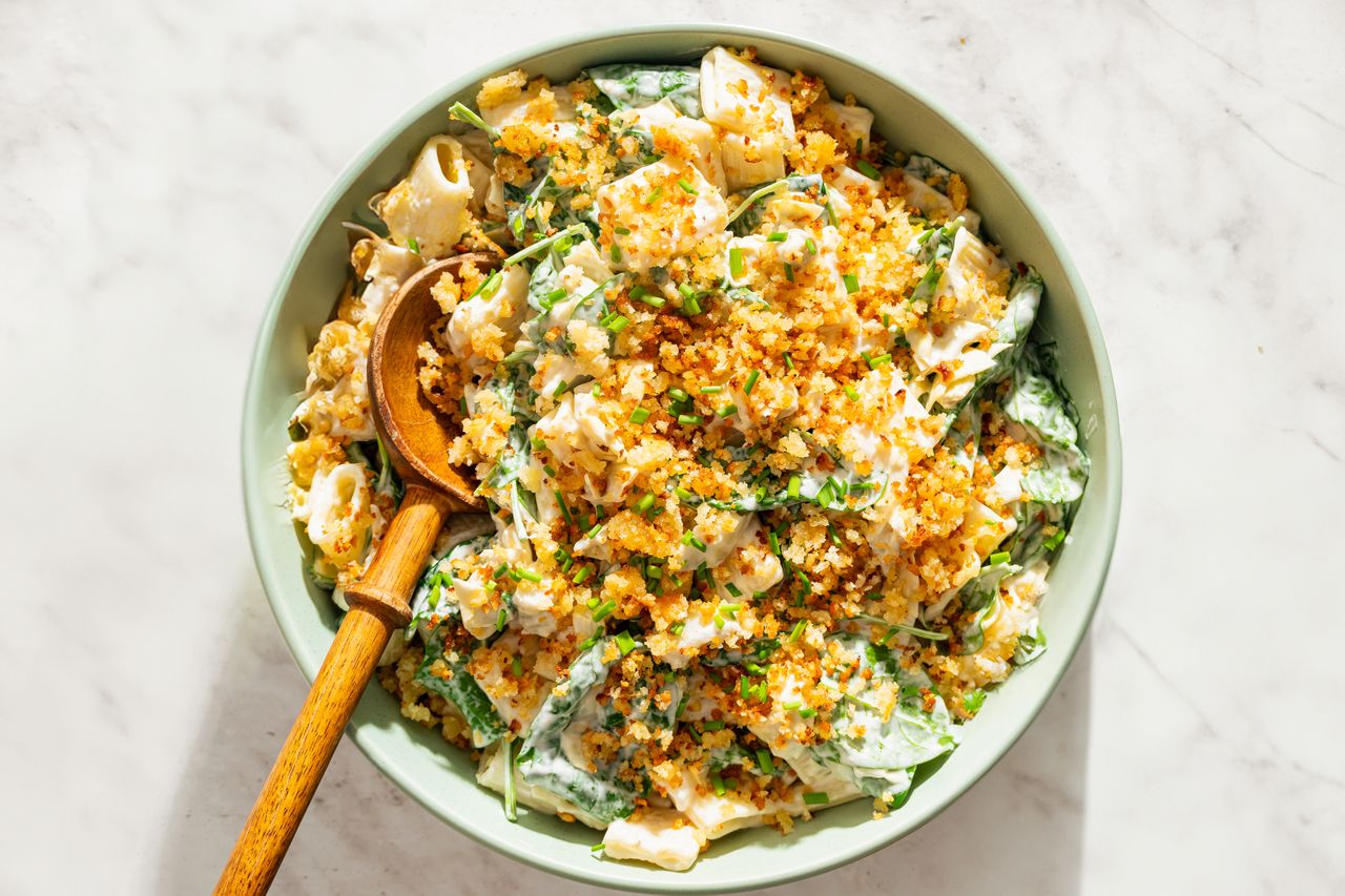 Bowl of spinach and artichoke pasta salad with a wooden spoon