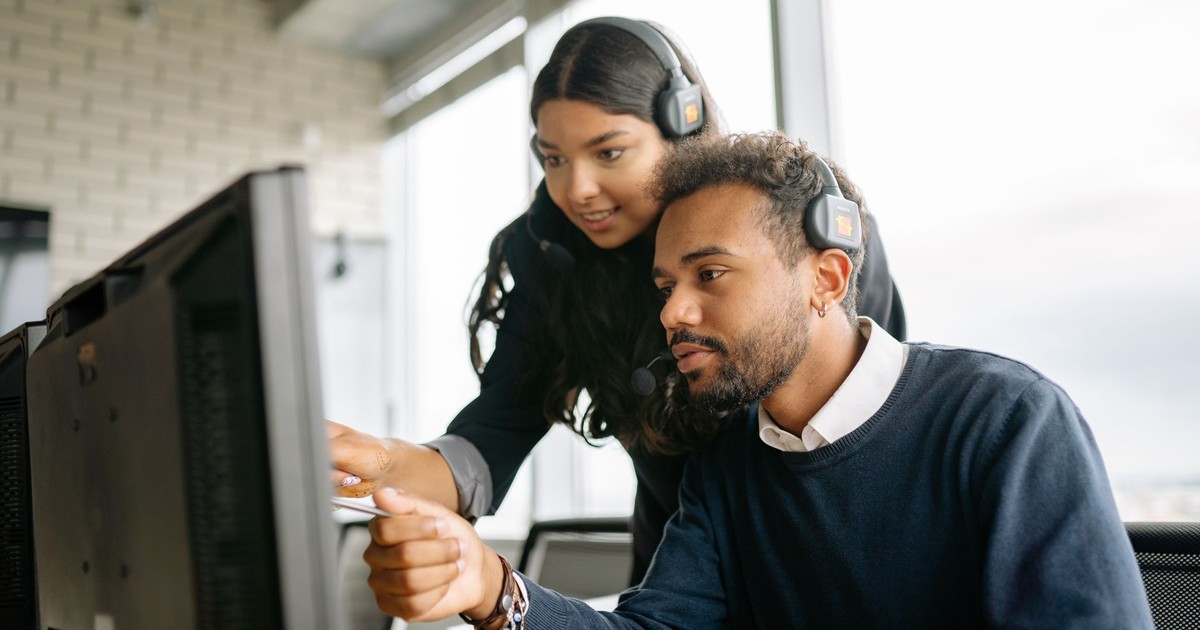 Two call center employees working together with headsets in a modern office setting.