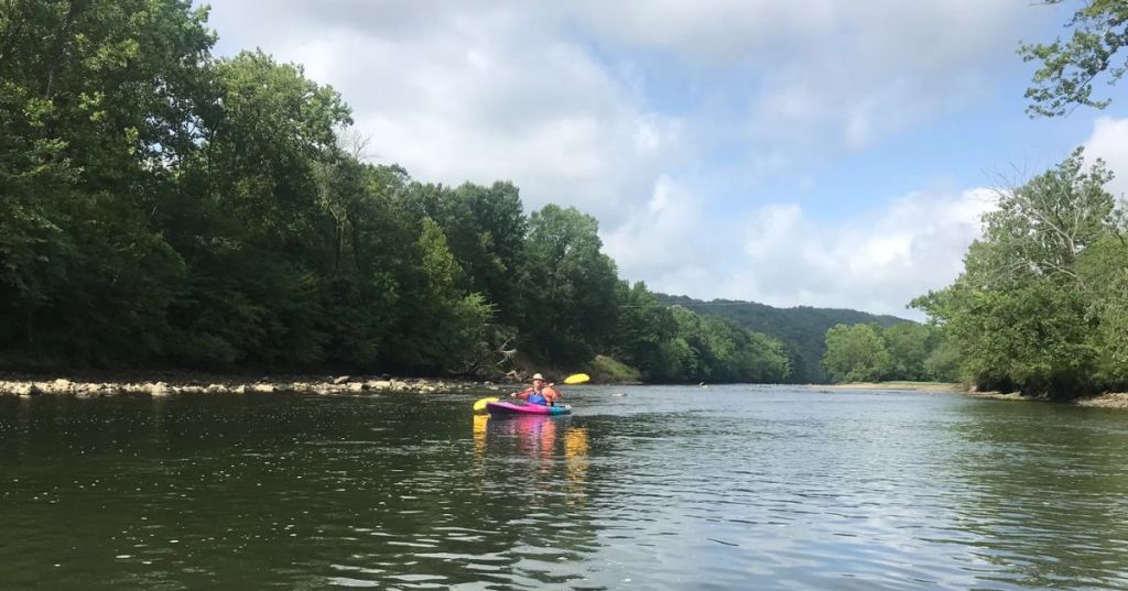 A kayaker paddling on the Ouachita River in Arkansas, surrounded by lush greenery.