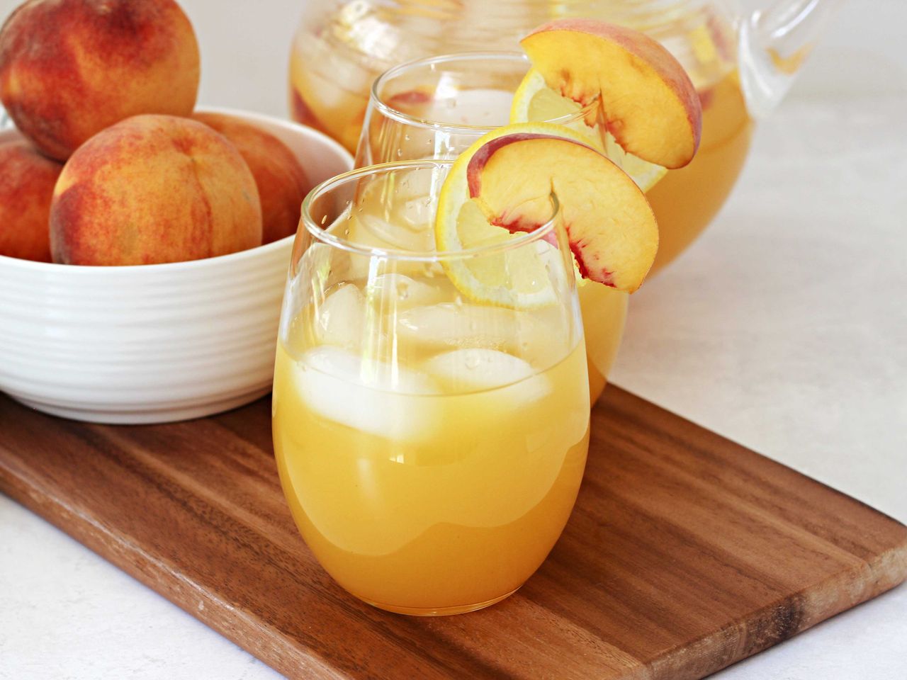 peach lemonade with ice and bowl of peaches in the background
