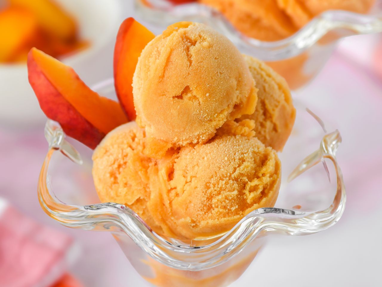 Scoops of peach sorbet in a glass dish with peach slices