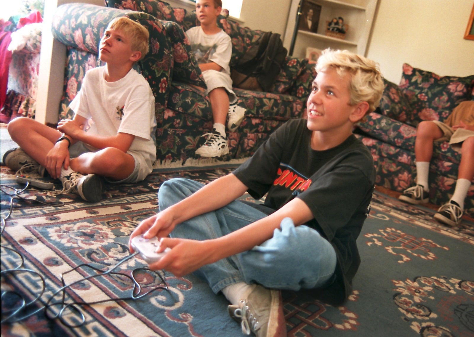 Teens seated on a living room floor playing video games, focused and engaged, with game controllers in hand. Casual, relaxed setting