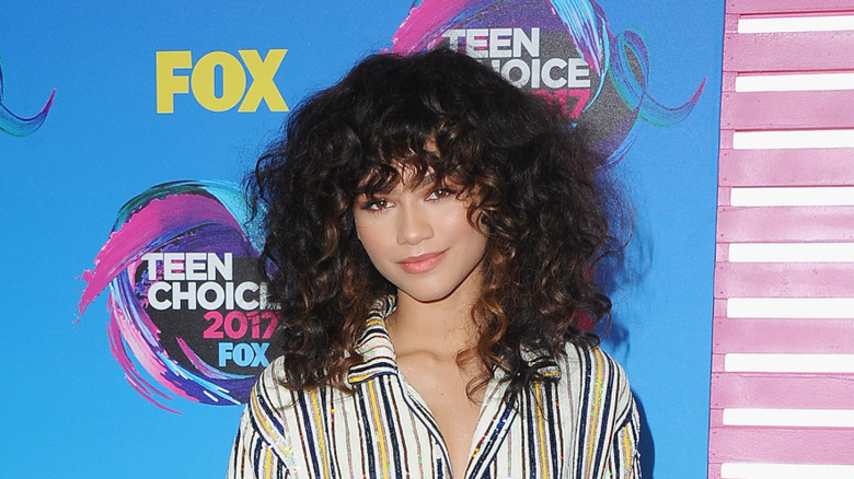 Zendaya posing at a red carpet event with curly hair wearing a striped shirt.
