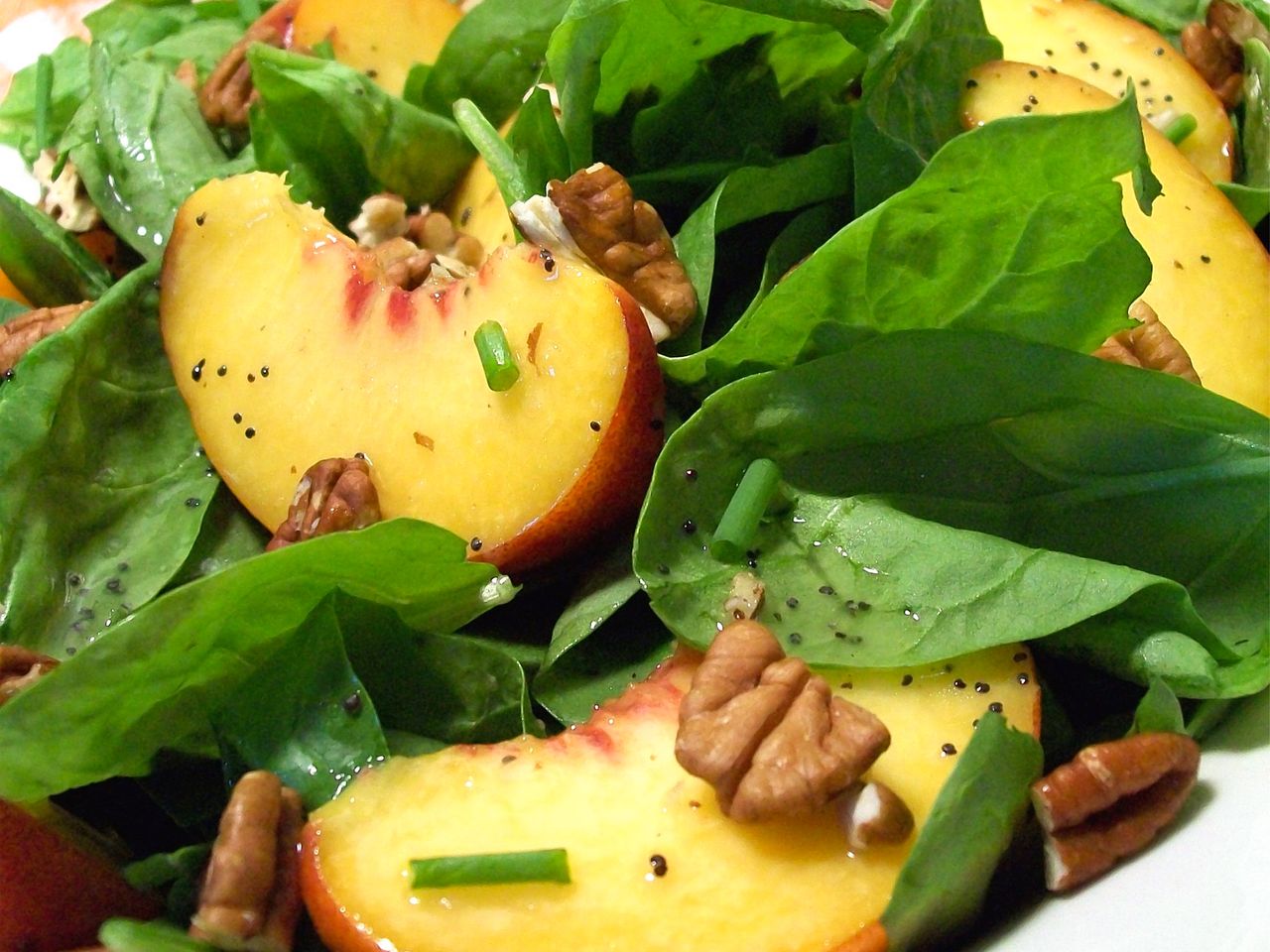 close up view of Spinach Salad with Peaches and Pecans with poppy dressing on a plate
