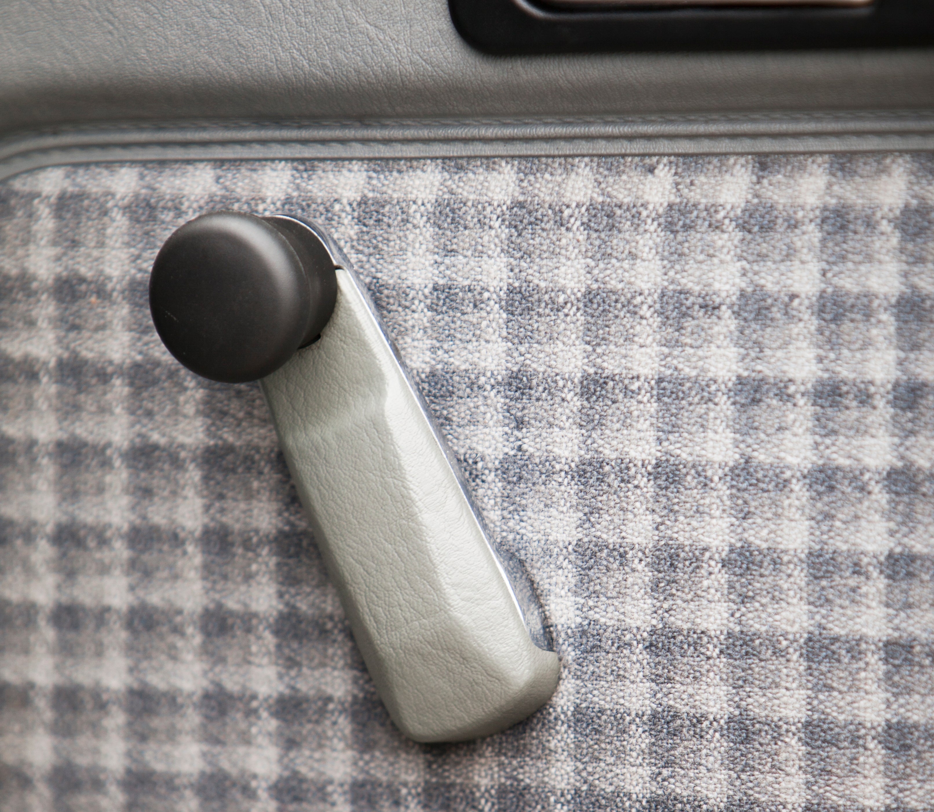 Manual car window crank handle on a plaid-patterned interior door panel