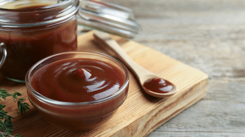 Homemade barbecue sauce in a glass ramekin, with a wooden spoon beside it