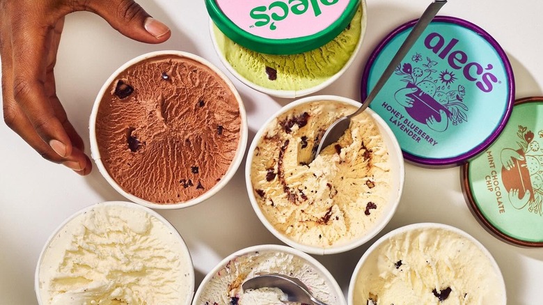 Aerial shot of various Alec's Ice Cream flavors in open pints, with a hand reaching for one.