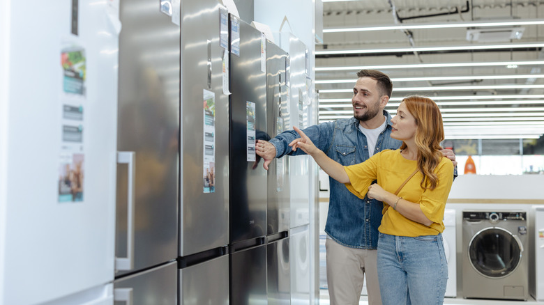 A couple is looking at a stainless steel fridge in a store