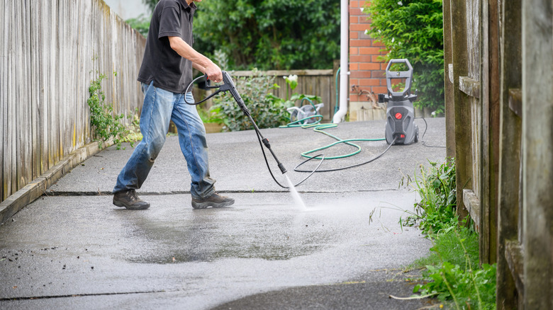 Man washing concrete driveway using pressure washer