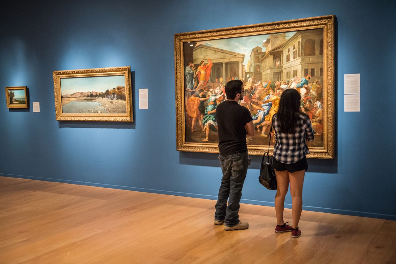 Two people standing in a museum gallery looking at a large painting on the wall