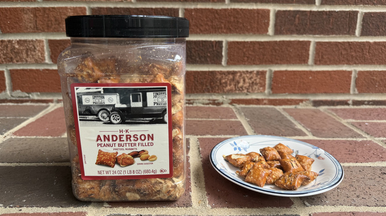 Medium plastic container of H.K. Anderson peanut butter-filled pretzels on brick surface, with some displayed on adjacent plate