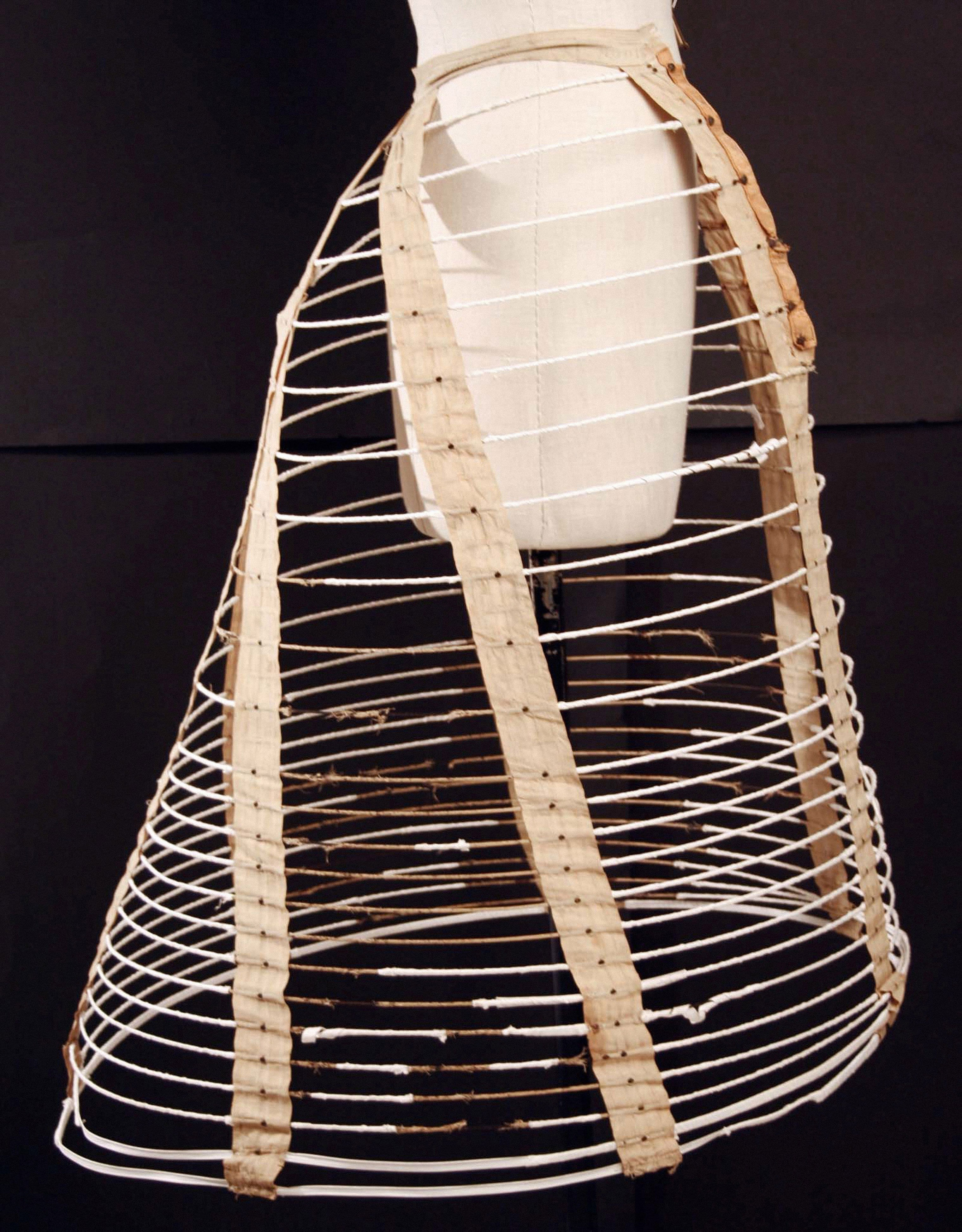 A vintage crinoline cage, showcasing its structure with metal hoops and fabric straps, displayed on a mannequin