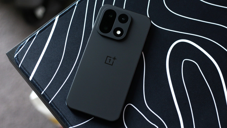 A black OnePlus 15 on a black-and-white deskmat