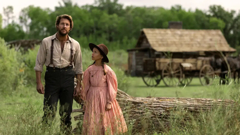 Charles and Laura Ingalls next to a log, a farmhouse behind them in Little House on the Prairie