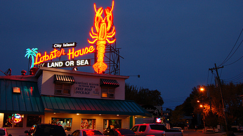 A large neon light sign is illuminated over a seafood restaurant and cafe at night on City Island, New York
