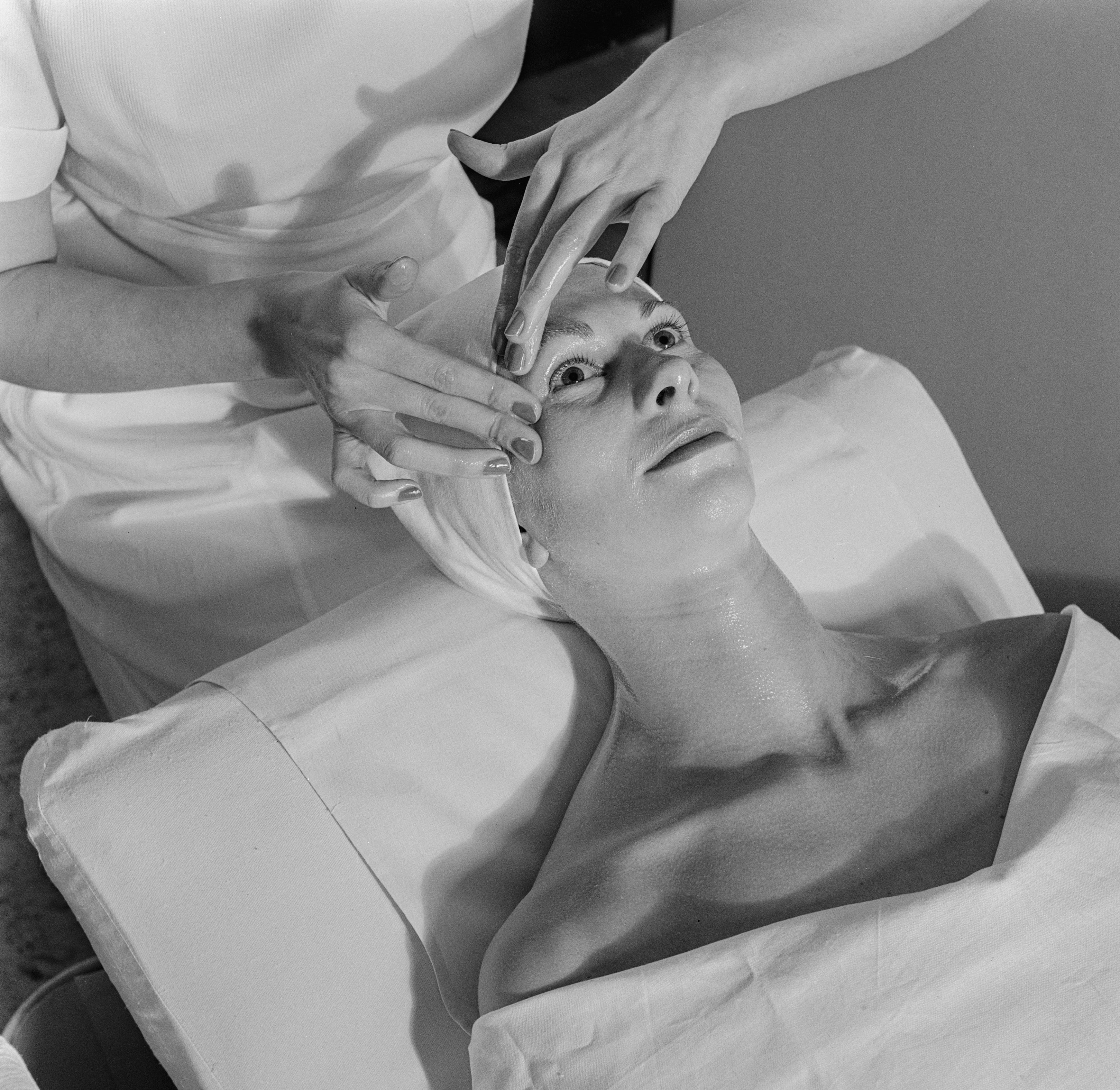 Person receiving a facial treatment, lying on a table with a towel, as an esthetician gently massages their face