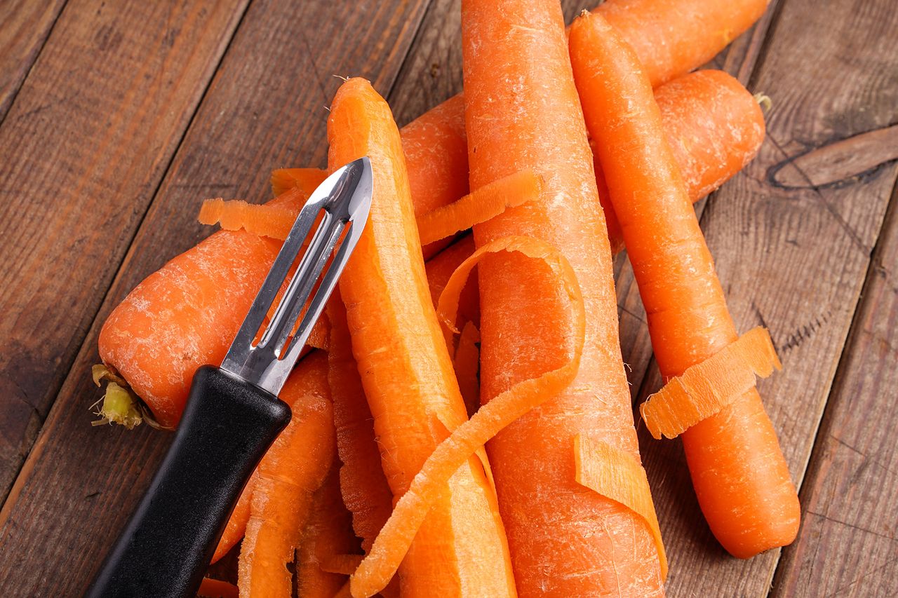 peeled carrots with peeler on wooden background