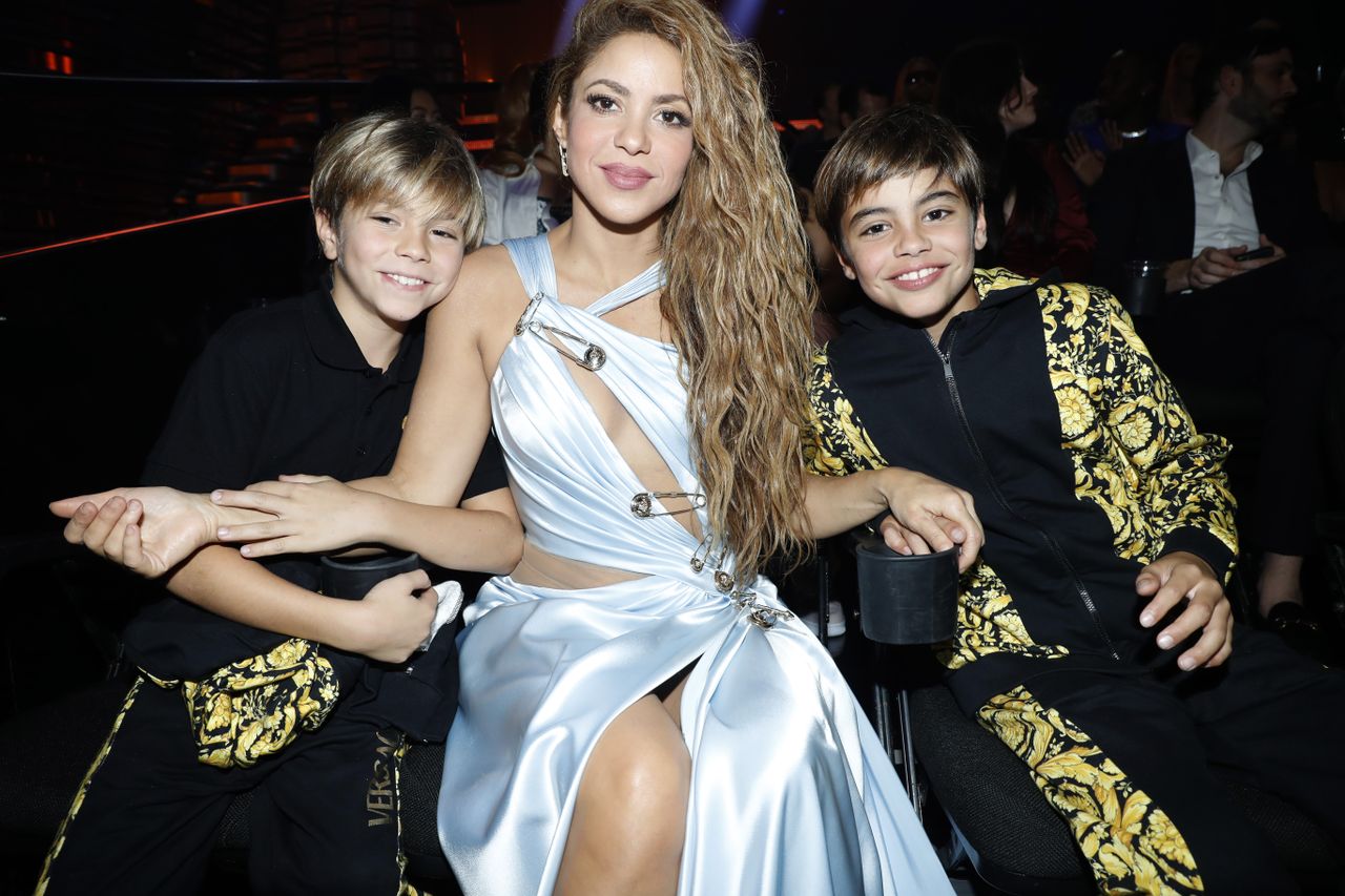 Shakira sitting in between her two sons wearing a blue gown held together by giant safety pins
