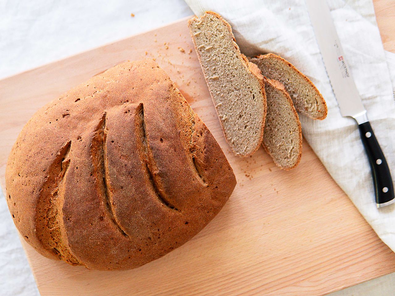 Homemade German loaf of bread on wooden board, knife and 3 bread slices