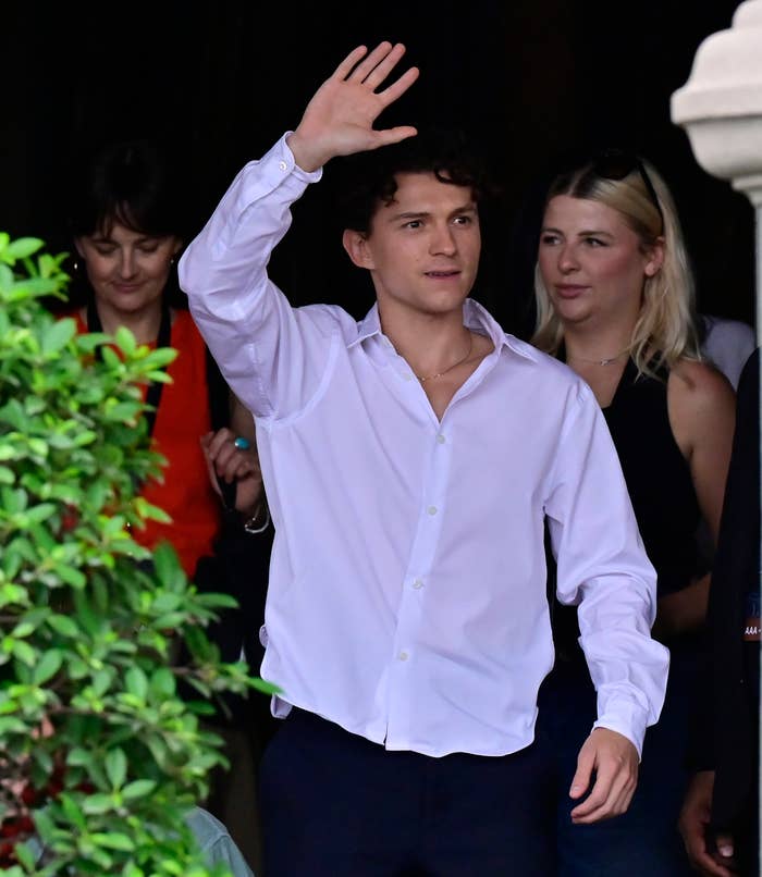 Person in a formal shirt waves to a crowd, accompanied by others