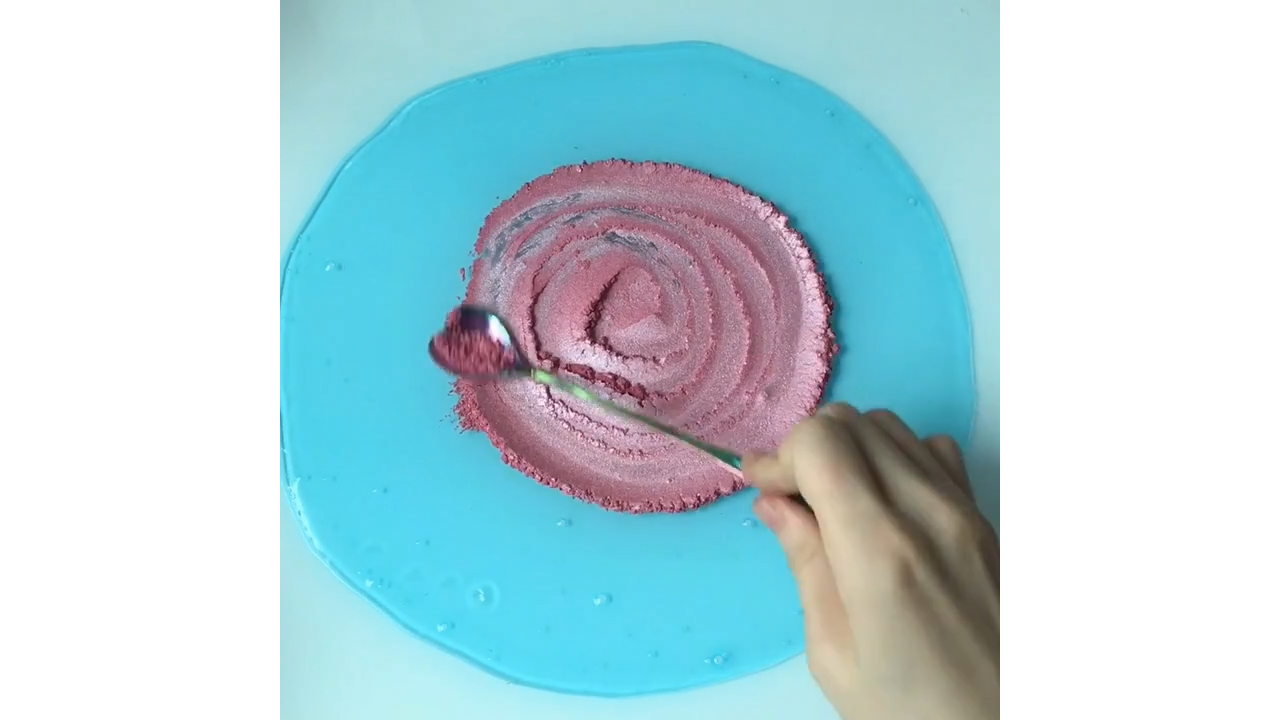 Pink kinetic sand scooping through crystal clear blue slime