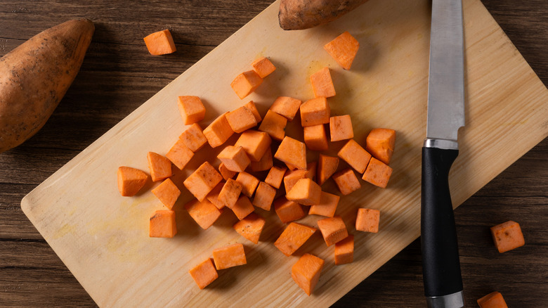 Cubed orange sweet potato chunks on a cutting board next to knife