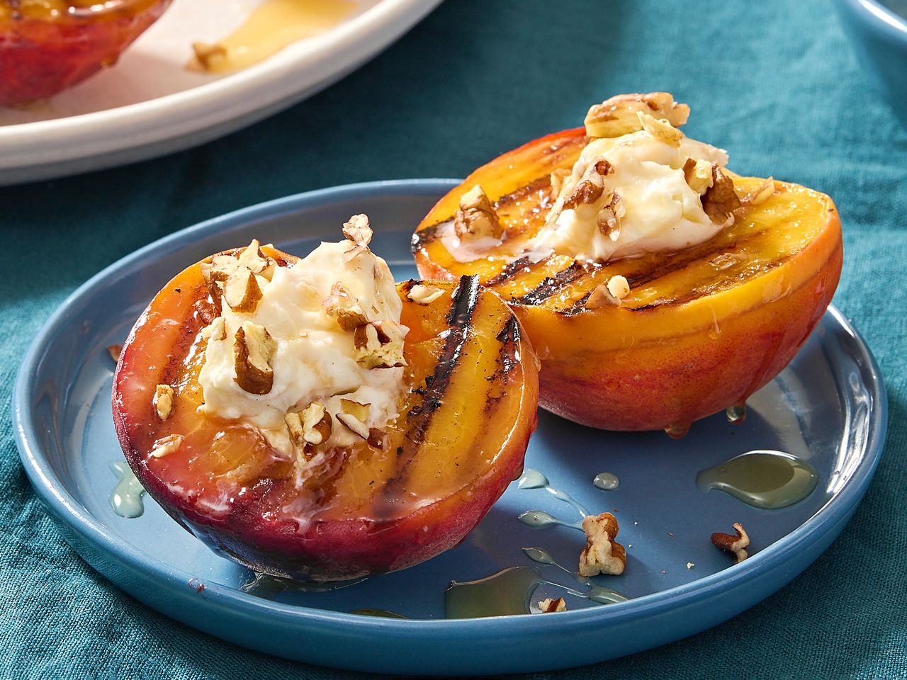 Grilled peaches topped with cream and nuts served on a plate