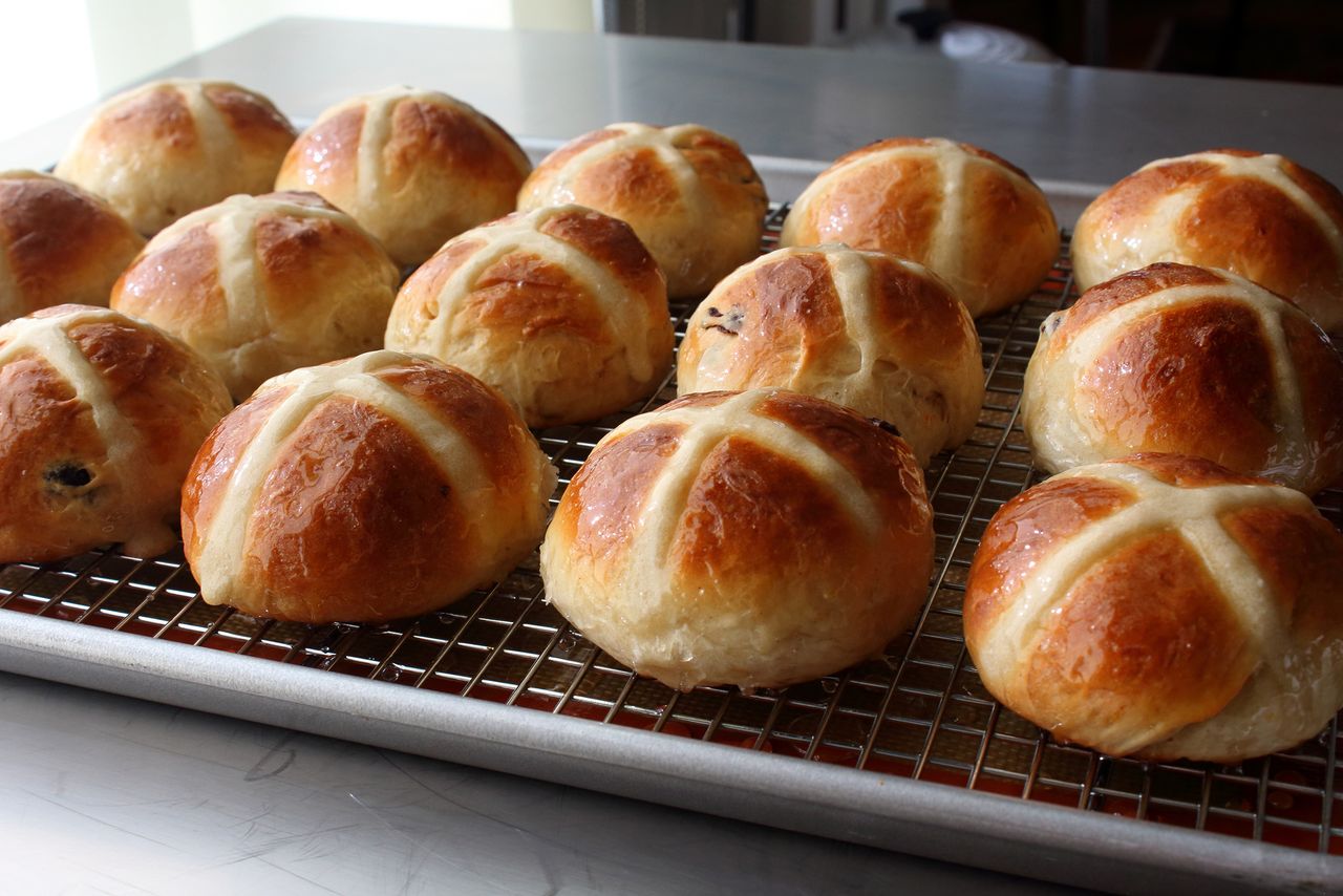 A tray of baked buns with cross patterns on top placed on a cooling rack