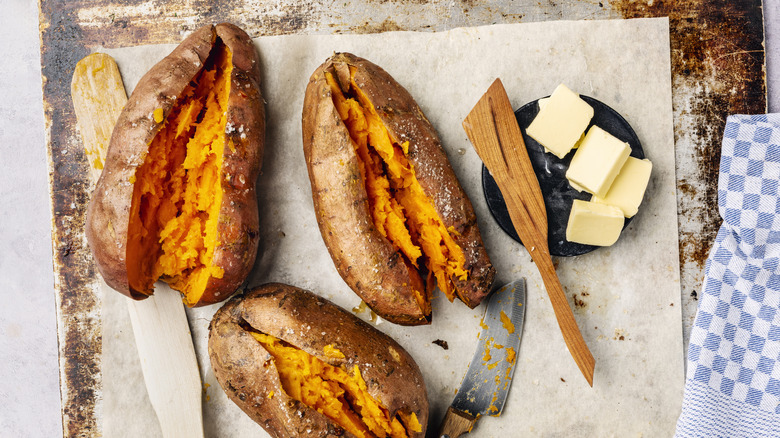 Three roasted sweet potatoes cut in half with butter and knives alongside