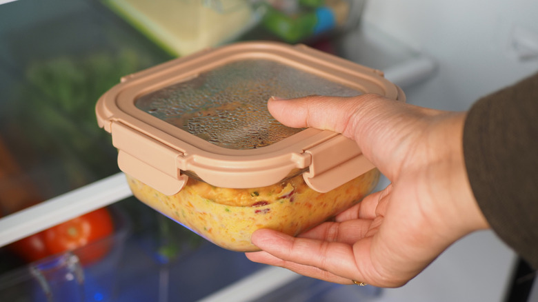Removing a plastic container of leftovers from the fridge