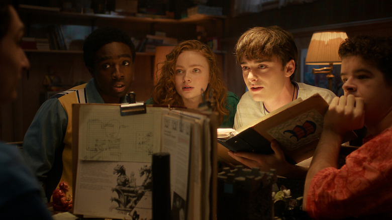 Finn Wolfhard as Mike, Caleb McLaughlin as Lucas, Sadie Sink as Max, Noah Schnapp as Will, and Gaten Matarazzo as Dustin sitting around a table playing D&D in Stranger Things 5