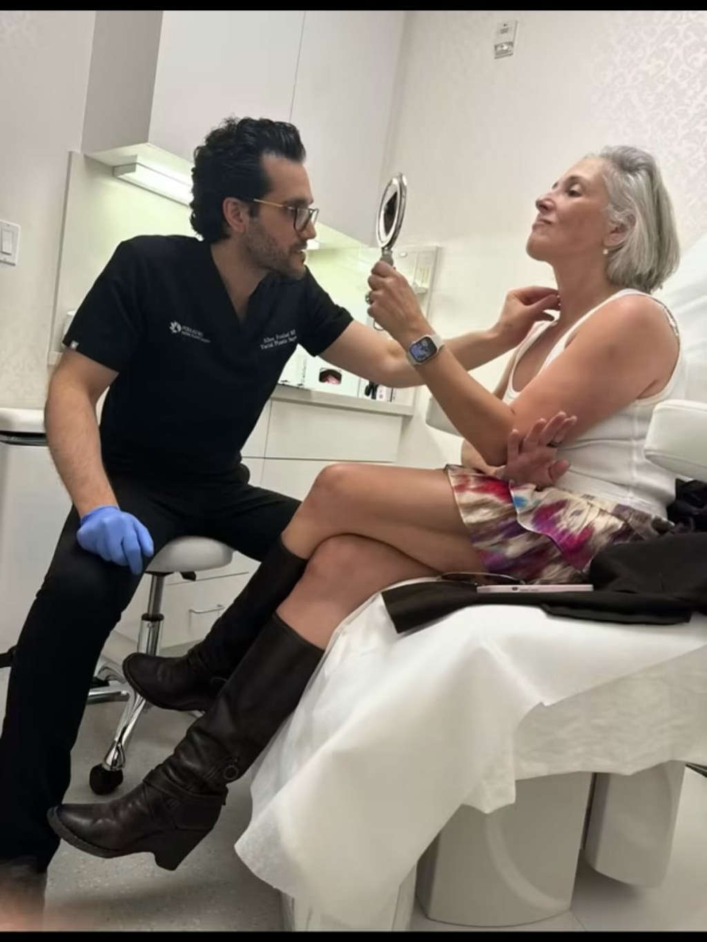 Ricki Lake in a consultation for a facelift, with a doctor holding a mirror for her to examine her neck.