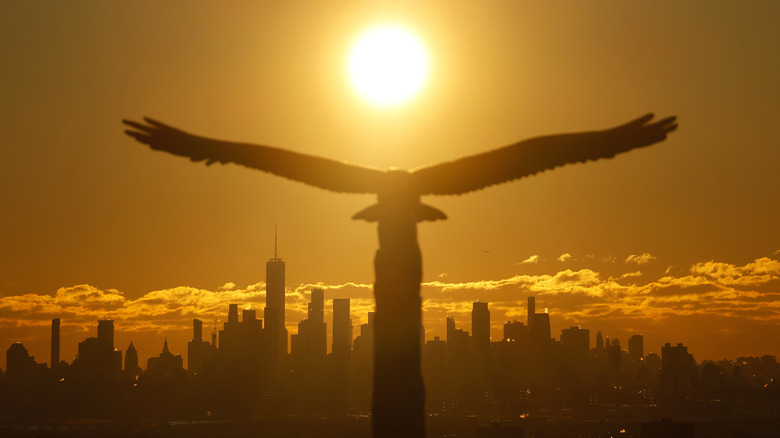 The sun rises behind the skyline of lower Manhattan and One World Trade Center in New York City and a statue of an eagle at Eagle Rock Reservation on January 21, 2024