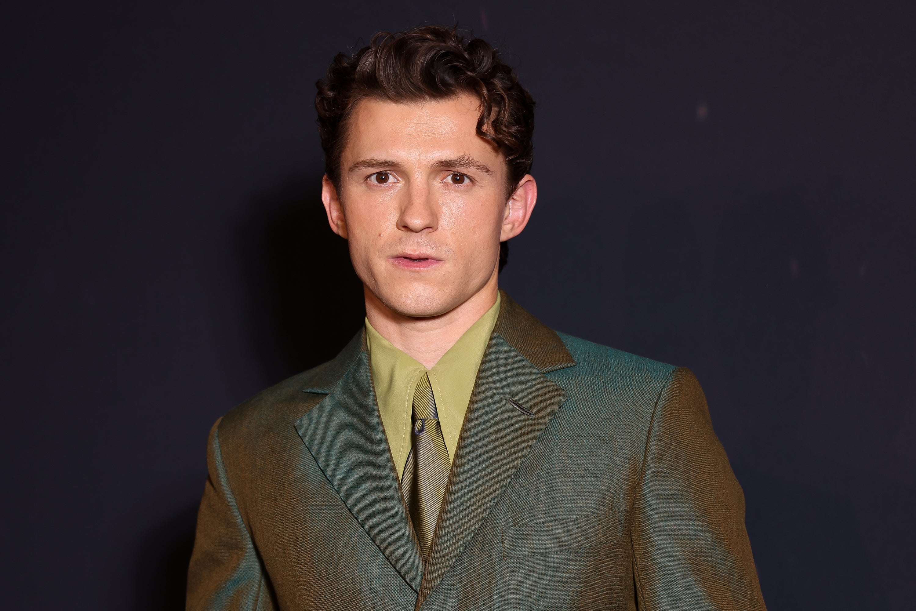 Man in a tailored suit with a collared shirt and tie, posing against a dark backdrop