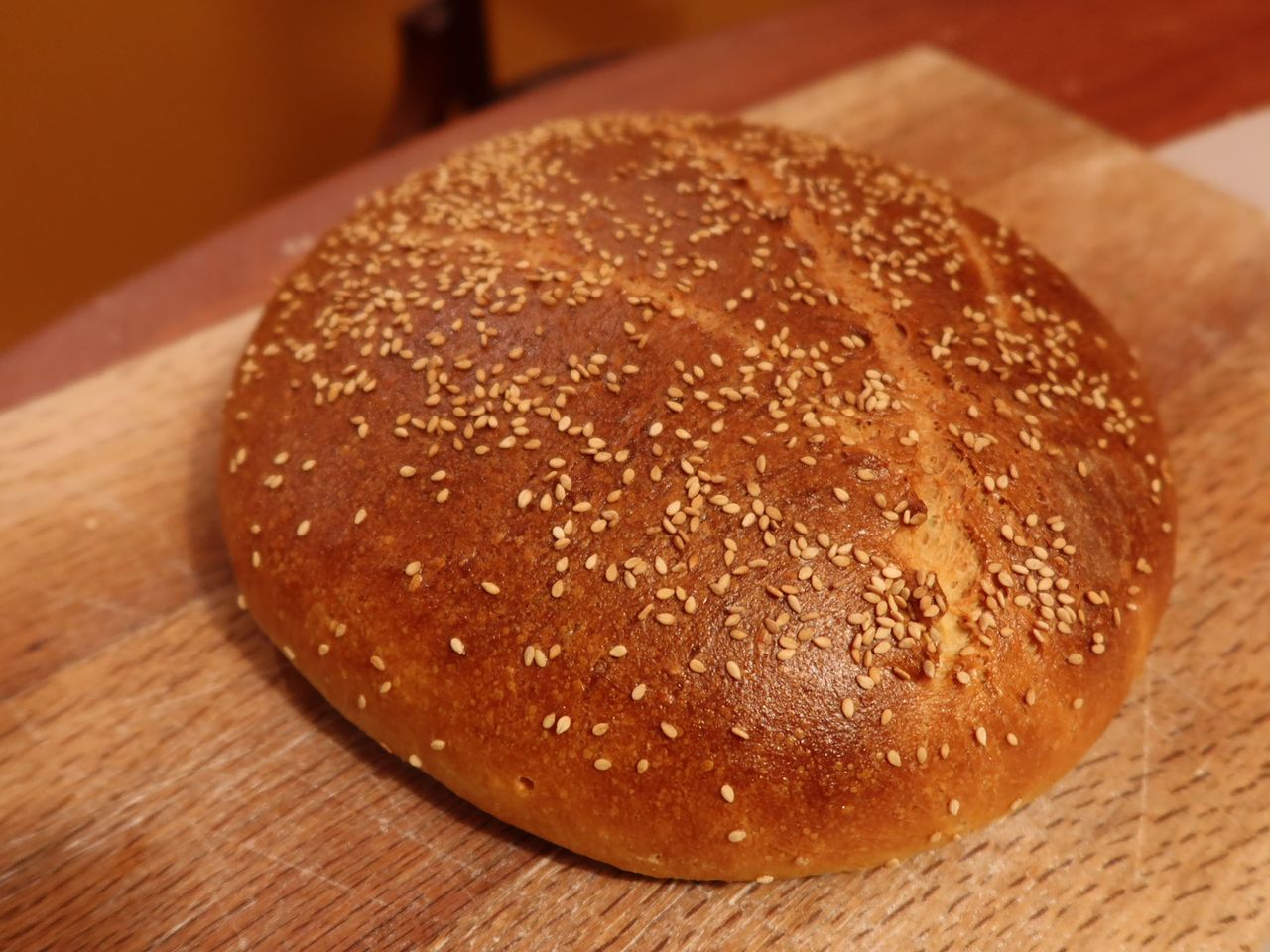 a round loaf of bread with a glossy brown crust topped with sesame seeds - Khobz el Dar (Algerian Semolina Bread)