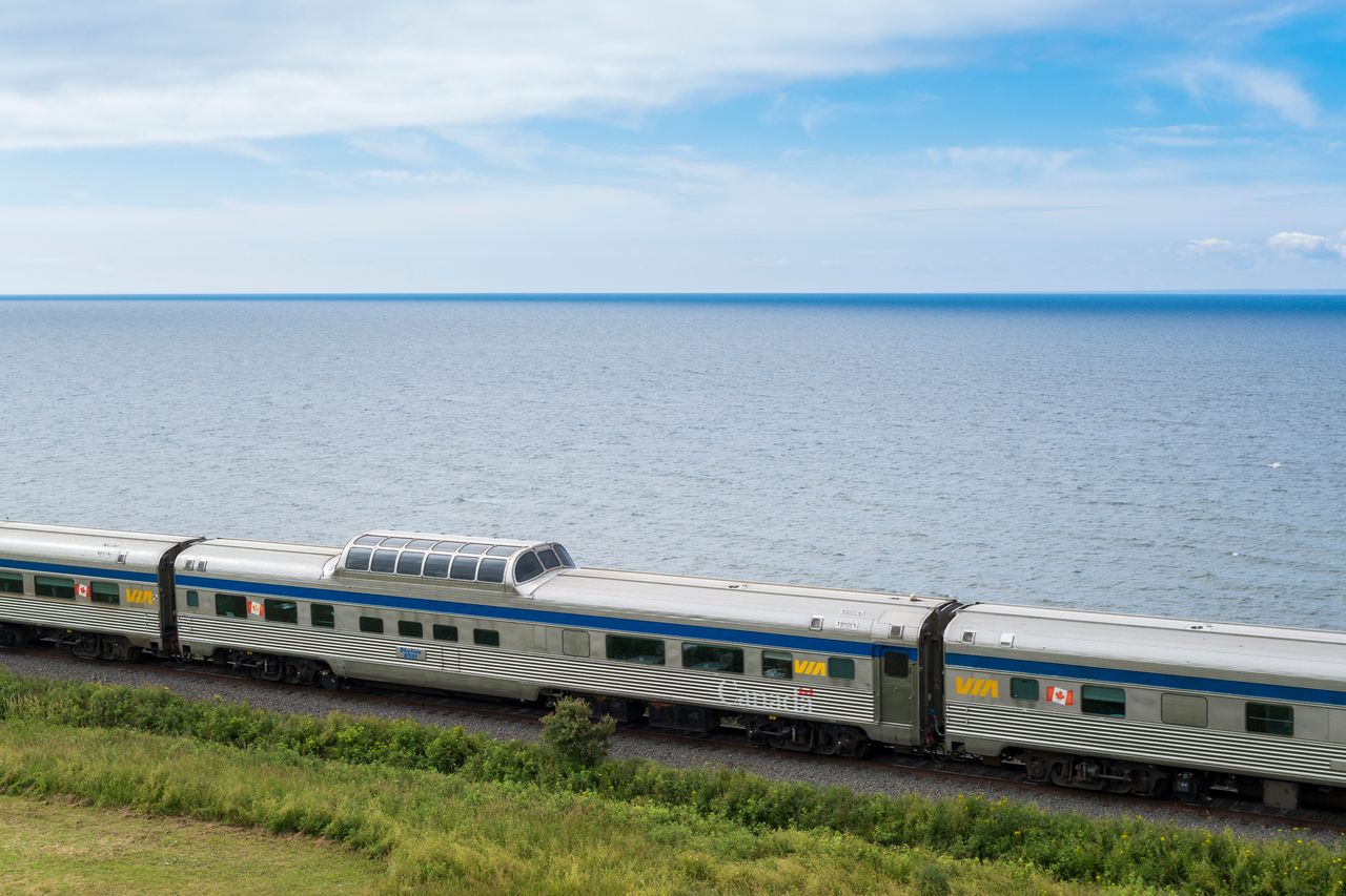 A train traveling along a body of water in a scenic area possibly a VIA Rail service