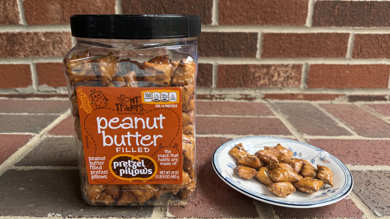 Medium plastic container of HT Traders peanut butter-filled pretzels on brick surface, with some displayed on adjacent plate
