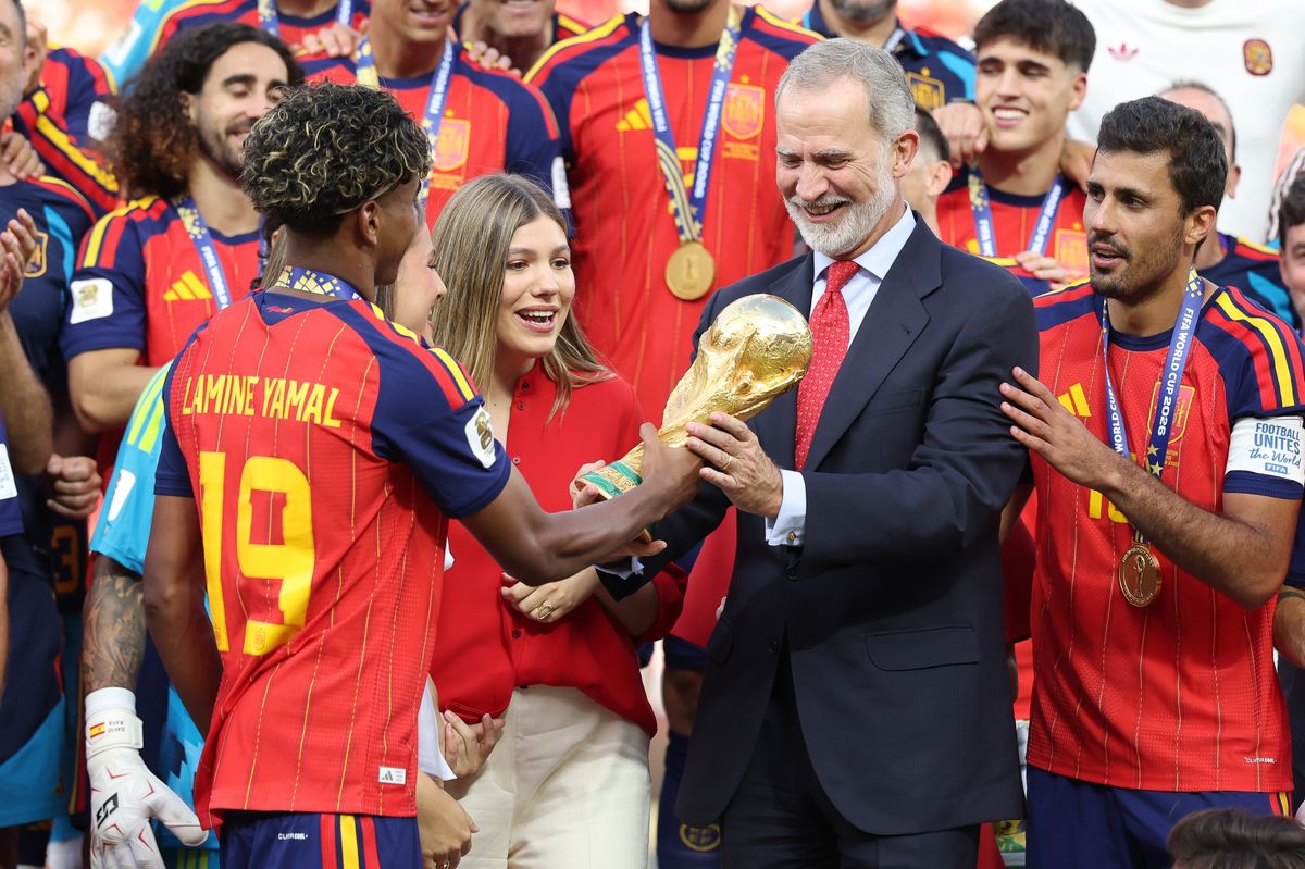 Lamine Yamal presents the FIFA World Cup trophy to King Felipe VI as Queen Letizia, Princess Leonor, Infanta Sofía, and Spain's players celebrate their historic victory.