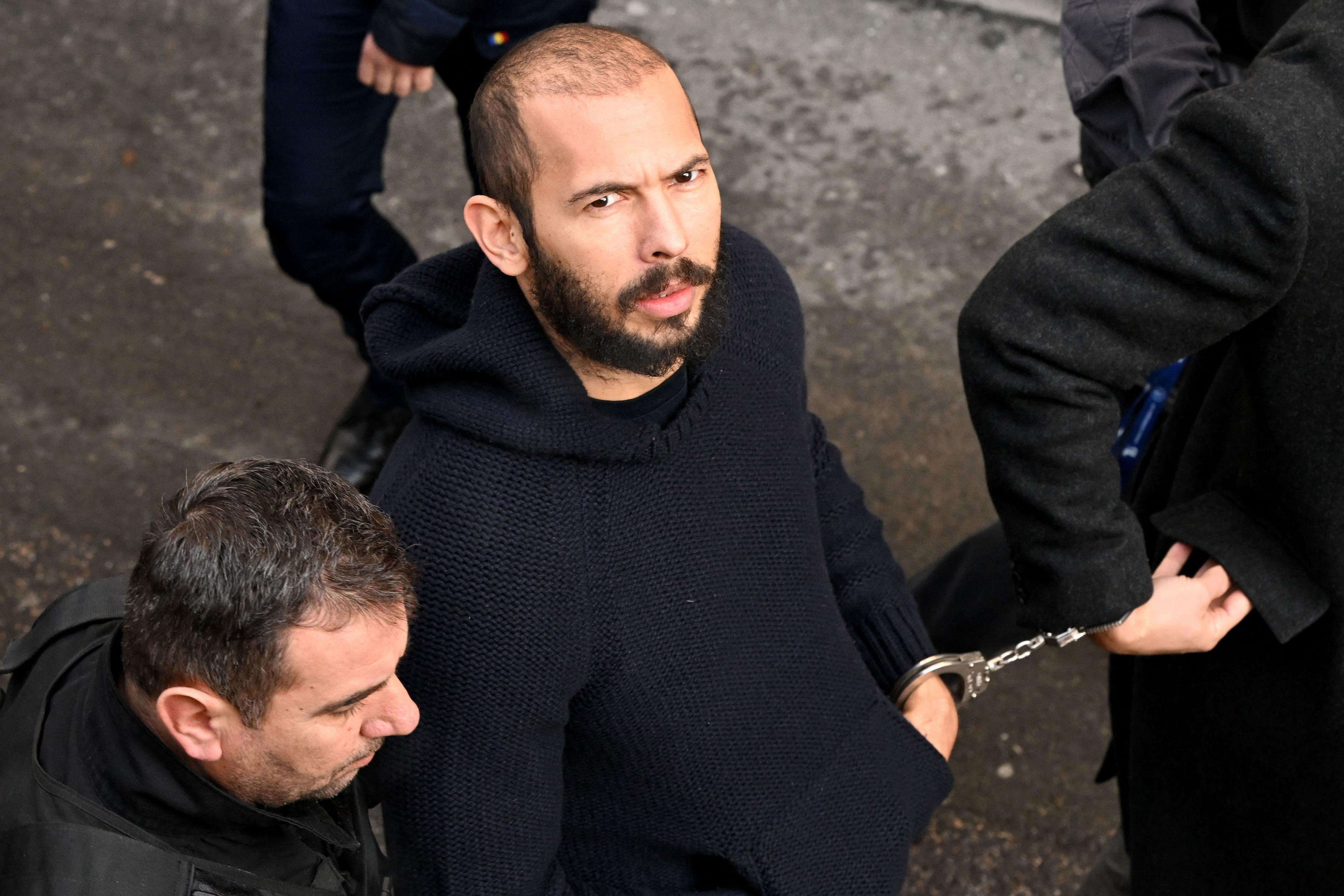 Andrew Tate arrives handcuffed and escorted by police at a courthouse in Bucharest on February 1, 2023. / DANIEL MIHAILESCU / AFP via Getty Images